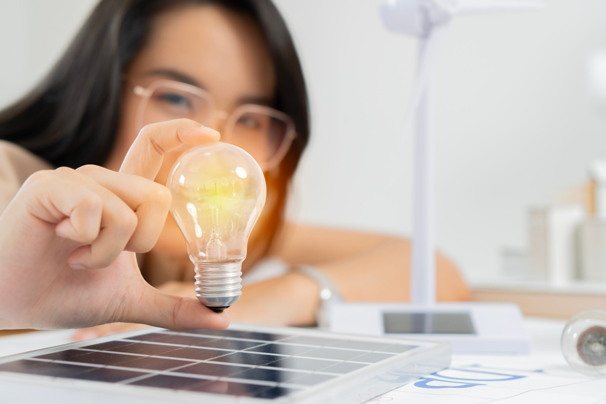 Facilitator sits at a table, holding a light bulb that is lit up over a solar panel. 